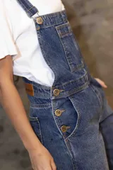 Enterito de denim azul con silueta relajada, breteles regulables, peto con bolsillo frontal y piernas rectas con tajos laterales en el ruedo.