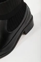 Bota de caña media combinada, con puntera y talón en cuero negro y caña de tejido de punto acanalado elástico. Cuenta con taco cuadrado bajo y tirador trasero.