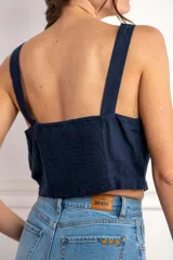 Top corto color rojo, con escote cuadrado y tirantes anchos. Presenta una hilera de botones marrones en el centro del frente.