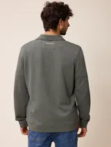 Buzo de polar color verde oscuro, con cuello polo y cierre frontal parcial. Presenta un pequeño bordado en el pecho y puños ajustados.