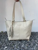 Cartera tote de cuero genuino color azul marino, con doble asa de hombro, costuras verticales y detalle de borla de flecos colgante.