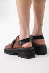 Sandalias de cuero color marrón con tiras cruzadas en blanco y negro, suela track y ajuste con velcro.