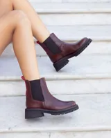 Botas tipo Chelsea de cuero color marrón, con paneles laterales elásticos en negro y tirador trasero en color rojo. Presentan una suela track robusta de goma negra con costuras decorativas en rojo.