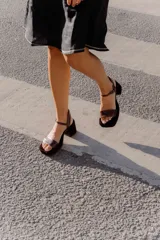 Sandalias de taco cuadrado medio, con base y talón en gamuza color tostado. Presenta una tira frontal de múltiples bandas doradas y una pulsera al tobillo con hebilla metálica.