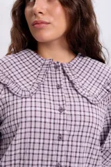 Camisa de manga larga con estampado a cuadros en tonos violeta y blanco, con cuello bobo grande con volados y cierre frontal de botones.