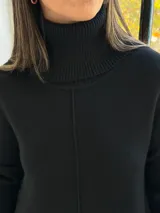 Sweater de punto color negro con cuello alto tipo polera, diseño holgado y corte asimétrico con la parte trasera más larga.