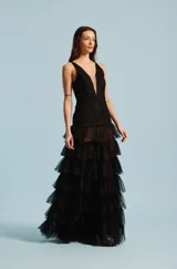 Vestido largo de fiesta color negro, con cuerpo bordado con apliques brillantes, escote en V profundo con inserción transparente, y falda escalonada de volados de tul.