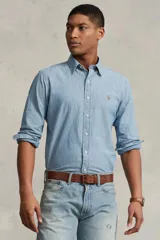 Camisa de hombre marca Polo Ralph Lauren, de manga larga, color celeste claro, confeccionada en tela chambray de algodón. Tiene cuello abotonado y logo bordado en el pecho.