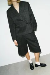 Blazer corto de corte oversize con estampado de cuadros, cuello con solapas de muesca y manga larga. Presenta cierre frontal cruzado con un botón y falsos bolsillos de vivo en el delantero. Incluye forro interior.