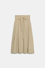 Falda midi color beige confeccionada en hilatura con mezcla de algodón. Presenta tiro medio, cintura con trabillas, bolsillos laterales ocultos en costura y cinturón del mismo tejido. Su diseño incluye un bajo acabado en línea evasé y cierre lateral con cremallera.