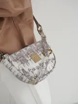 Bandolera de cuero color beige con correa ajustable y logo metálico dorado en el frente.