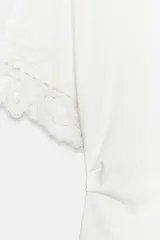 Camiseta negra de algodón con cuello redondo, manga corta y detalle de aplicación de encaje a tono en los puños. Presenta un diseño con bajo asimétrico y frunce lateral.