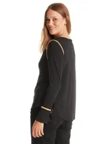 Blusa negra de crepe elastizado con ribetes en contraste color beige que recorren el escote en V, la línea central del frente y las costuras de los hombros. Tiene mangas largas con puños abiertos, abertura lateral y botón metálico.