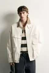 Parka relaxed fit de algodón color crudo, con cuello solapa marrón en contraste, múltiples bolsillos plastrón con solapa en el delantero y cierre frontal con cremallera y botones a presión.