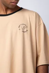 Remera de corte oversize en color beige, con cuello redondo en contraste negro y una manga en color negro. Presenta un pequeño estampado circular en el pecho con la frase 'Don't worry, be happy'.
