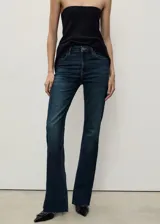 Jeans tiro medio de corte flare confeccionados en denim azul oscuro, con diseño de cinco bolsillos, trabillas para cinturón y bajo deshilachado.