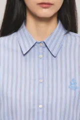 Camisa Sailor Line de calce holgado y diseño a rayas. Presenta cuello camisero, mangas largas y puños abotonados. Cuenta con acceso frontal mediante botones a tono y detalle bordado en el pecho.