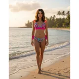Bikini de dos piezas con estampado floral tropical sobre fondo celeste. El corpiño es de estilo triángulo con volados naranjas en los breteles y una banda inferior fucsia con detalle de puntilla. La bombacha es de corte tanga con tiras laterales ajustables en color fucsia.
