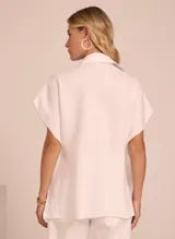 Camisa blanca de lino con cuello clásico, manga corta amplia, cierre frontal con botones y bolsillo de parche en el pecho.