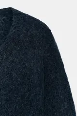 Jersey de punto con mezcla de lana y alpaca, color amarillo mostaza, con cuello en pico y manga larga. Presenta acabados en rib en puños y bajo.