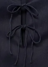 Vestido corto sin mangas con efecto denim, cuello redondo y detalle de lazos frontales. Presenta un diseño con tablas y cierre de cremallera en la parte posterior.