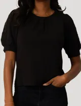 Blusa negra de corte recto con cuello redondo y mangas cortas abullonadas que presentan detalles calados con bordados en los hombros.