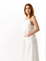 Vestido midi de lino color blanco, con escote recto, tirantes finos ajustables, cierre lateral y bolsillo frontal tipo parche.