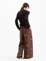 Pantalón de silueta holgada, color marrón, confeccionado en twill de algodón con estampa de flores amarillas y moras. Cuenta con bolsillos laterales y cierre frontal con botón y gancho.