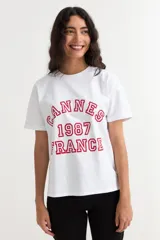 Remera de manga corta color beige, con estampa frontal en tono azul con la leyenda "New York 1990", de corte holgado y diseño casual.