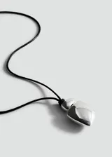 Collar largo con cordón negro ajustable y dije metálico de diseño orgánico y minimalista.