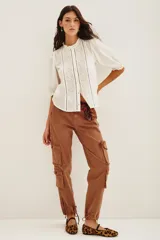 Camisa blanca de algodón con cuello alto tipo gorguera, mangas abullonadas y cierre frontal con botones. Presenta un diseño con paneles verticales de encaje bordado con motivos de corazones y detalles calados.