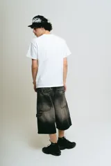 Bermuda de jean estilo carpintero, corte baggy, color negro lavado con efecto degradado. Presenta bordados en la parte trasera con tipografía gótica que dice "Lucca Bossio". Incluye bolsillos grandes y bolsillo lateral de carpintero.