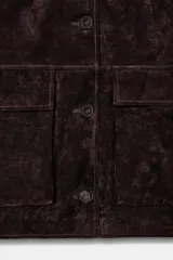 Cazadora de ante color marrón oscuro, con cuello solapa, manga larga y cierre frontal de botones. Incluye dos bolsillos delanteros de plastrón con solapa.