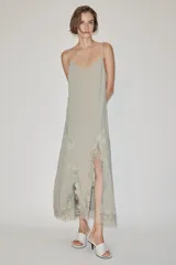 Vestido largo lencero de tejido fluido en color gris verdoso, con escote en V, tirantes finos y detalles de encaje a tono en el bajo y los laterales, además de una abertura frontal.