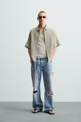 Camisa de manga corta con cuello solapa, confeccionada en tejido de mezcla de lyocell con textura de efecto arrugado y cierre frontal de botones.