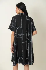 Camisa larga negra con estampado de líneas geométricas en gris, de manga corta y dos bolsillos delanteros.