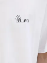 Remera de corte holgado color blanco, con cuello redondo y manga corta. Presenta una estampa artística en la espalda con motivos de playa, sombrilla y silla de descanso.