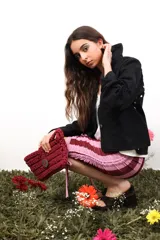 Bolso de mano tejido a crochet en trapillo grueso color verde oscuro, con un botón metálico grande y redondo con el logo de la marca CAPER en rojo.