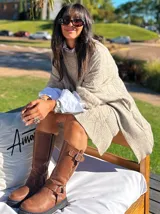 Poncho de tejido de punto con diseño de ochos, color beige, con cuello redondo y mangas amplias que presentan detalles de puños de piel sintética.