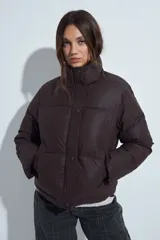 Campera puffer de nylon color marrón oscuro, con cuello alto, cierre frontal y puños elásticos. Diseño acolchado de volumen ligero.