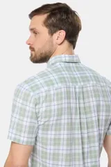 Camisa de manga corta confeccionada en lino, con diseño de cuadros en tonos verdes y blancos, cuello camisero y cierre frontal de botones.