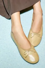 Zapato tipo bailarina plana confeccionado en piel, con detalle de lazo decorativo en la parte frontal y punta redonda.