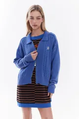 Cardigan de tejido de punto color marrón, con cuello solapa, cierre frontal de cremallera y diseño de trenzas. Cuenta con puños y dobladillo en rib elástico y un pequeño bordado en el pecho.