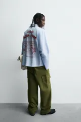 Camisa de algodón de corte regular, color celeste con finas rayas blancas verticales. Presenta un bordado en color rojo en el pecho con la frase "Café du Matin Doux".