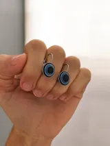 Caravanas con diseño de ojo turco circular, con centro negro rodeado de anillos en tonos azul y blanco, montadas en base de acero quirúrgico con cierre tipo gancho.