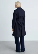 Trench coat de corte recto y diseño cruzado en color azul oscuro. Presenta cuello de solapa, cierre frontal de botones efecto carey, cinturón ajustable en la cintura, trabillas en los puños y dos bolsillos laterales. Cuenta con abertura posterior en el bajo y acabado repelente al agua.