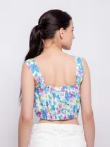 Top blanco con estampado floral en tonos naranja y lila, de corte cropped y breteles anchos.