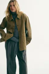Campera camisera de sarga de algodón verde militar con cuello clásico, cierre frontal de botones y dos bolsillos delanteros de parche. Cuenta con hombros caídos, mangas largas con puños abotonados y bajo recto con aberturas laterales redondeadas.