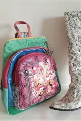 Mochila de cuero multicolor con diseño texturizado, que combina tonos fucsia, verde, azul y rosa. Cuenta con bolsillo frontal con cierre y arte abstracto pintado, además de manija superior y correas ajustables.