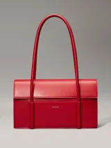 Cartera de hombro Calvin Klein estructurada, color rojo vibrante, con solapa frontal y bolsillo exterior con el logo grabado en metal plateado. Posee asas tubulares superiores y una correa ajustable para llevar cruzada.